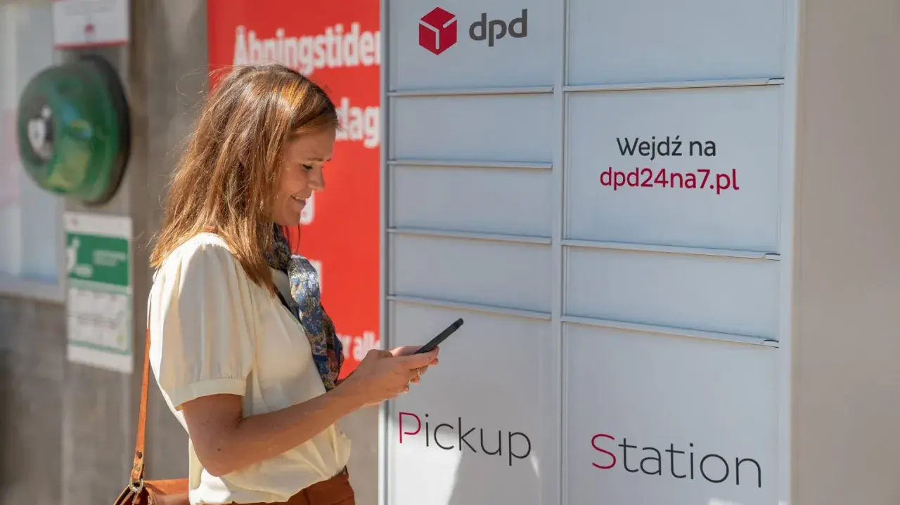 Kobieta z telefonem przy automacie DPD Pickup Station. Możliwe, że zarządza dpd przekierowanie paczki.