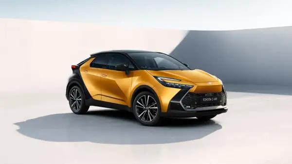 Nowy Toyota C-HR Hybrid w kolorze złotym, z czarnym dachem i felgami, prezentuje się nowocześnie na tle białej ściany.