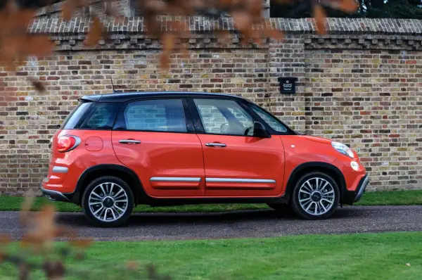 Pomarańczowy fiat 500xl z czarnym dachem stoi na tle ceglanej ściany.