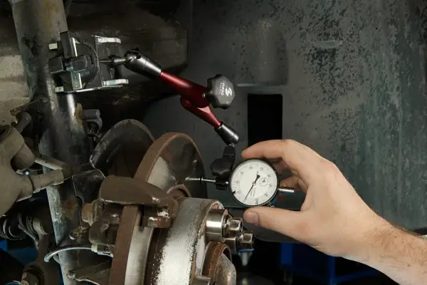 Mechanik mierzy bicie tarczy hamulcowej, by zdiagnozować drgania kierownicy przy hamowaniu z dużej prędkości.