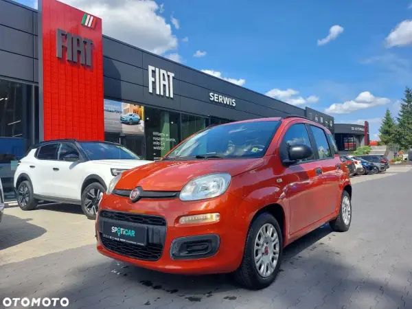 Pomarańczowy fiat panda używany z salonu czeka na nowego właściciela. Obok biały SUV.