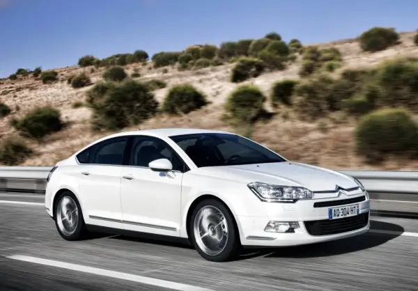 Biały Citroen C5 z hydropneumatycznym zawieszeniem jedzie po drodze. Zastanawiasz się nad citroen c5 zawieszenie hydropneumatyczne koszt naprawy?