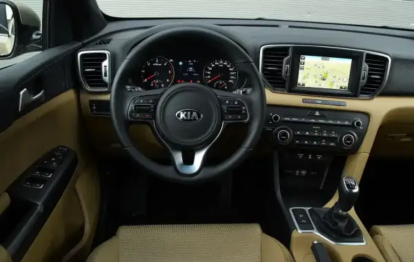Wnętrze Kia Sportage IV z beżową tapicerką, multimediami z nawigacją i wielofunkcyjną kierownicą.