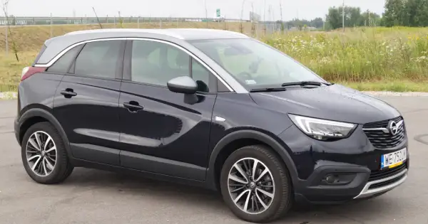 Ciemnogranatowy Opel Crossland z dwukolorowym dachem, stojący na tle łąki. Wady i zalety tego modelu to temat dyskusji.