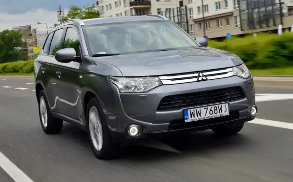 Szary Mitsubishi Outlander 3 jedzie po miejskiej drodze.