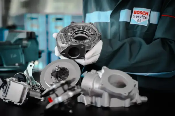 Mechanik w białych rękawiczkach prezentuje części turbiny. Na stole leżą wirnik i obudowa, gotowe do montażu.