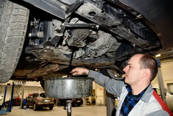 Mechanik spuszcza stary olej z silnika, przypominając o regularnej wymianie oleju dla sprawnego działania auta.