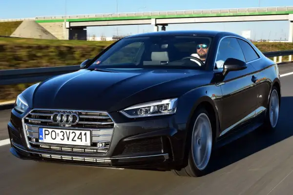 Czarny Audi A5 F5 z kierowcą w okularach przeciwsłonecznych jedzie autostradą.