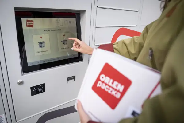 Kobieta z paczką ORLEN Paczka dotyka ekranu automatu paczkowego, wybierając opcję nadania przesyłki.