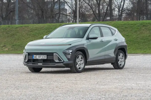 Nowy Hyundai Kona 1.6 benzyna w pastelowym kolorze, zaparkowany na żwirowym placu, gotowy na miejskie przygody.