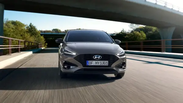 Nowy Hyundai i30 2023 w kolorze brązowym jedzie po moście wśród zieleni.