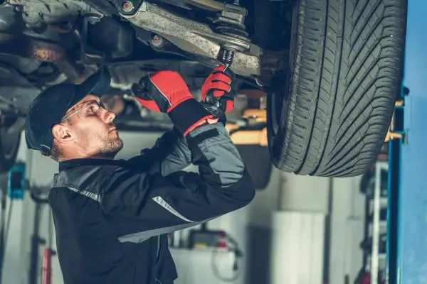 Mechanik w rękawicach dokręca sworzeń zwrotnicy w podwoziu samochodu.