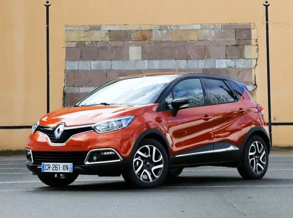 Pomarańczowy Renault Captur 2016 z czarnym dachem stoi przed ceglaną ścianą.