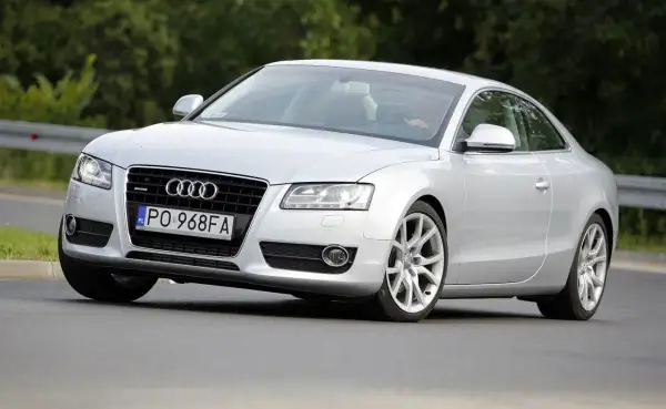 Srebrne Audi A5 z 2006 roku na drodze, z widocznym kierowcą.