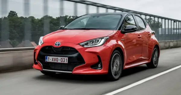 Czerwony Toyota Yaris 1. generacji z czarnym dachem pędzi po drodze.