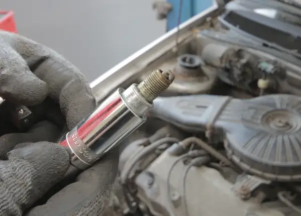 Ręka w rękawicy trzyma świecę zapłonową, potencjalną przyczynę błędu DTC P0301 w Volvo.