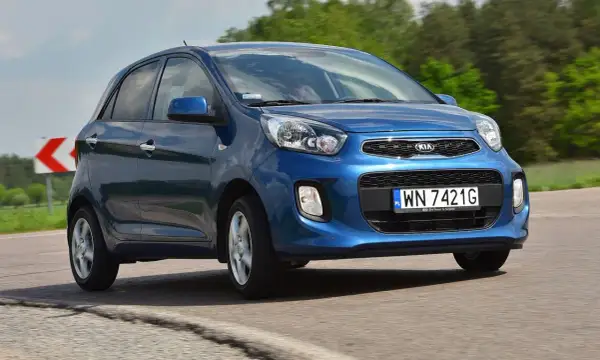 Niebieski Kia Picanto 2012 na drodze, z zielonymi drzewami w tle.