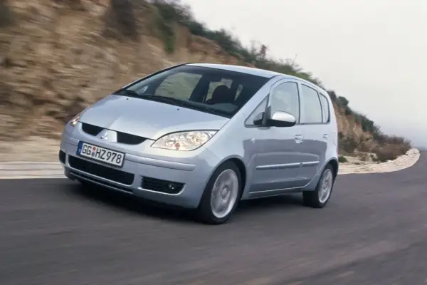 Srebrny Mitsubishi Colt VI pokonuje zakręt na krętej drodze, otoczony przez wzgórza.