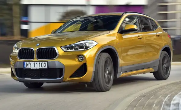 Złoty BMW F39 w ruchu, z widocznym grillem i reflektorami.