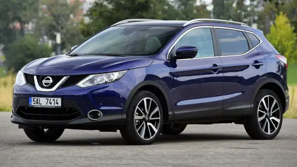 Granatowy Nissan Qashqai J11 z chromowanymi relingami dachowymi i felgami stoi na drodze.