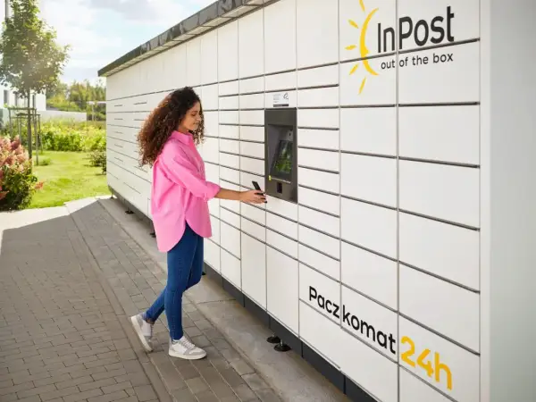 Kobieta z telefonem przy Paczkomacie InPost. Szybka wysyłka paczek za granicę jest teraz prosta.