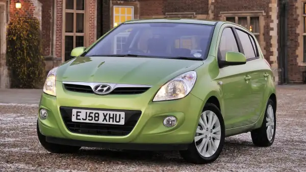 Zielony Hyundai i20 z włączonymi światłami przeciwmgielnymi przednimi, zaparkowany przed ceglanym budynkiem.