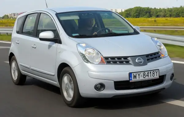 Srebrny Nissan Note E11 jedzie po drodze, za kierownicą siedzi mężczyzna.