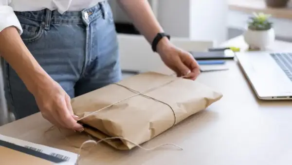 Ręce wiążą sznurkiem paczkę owiniętą w papier. Gdzie nadać mini paczkę Poczta Polska?