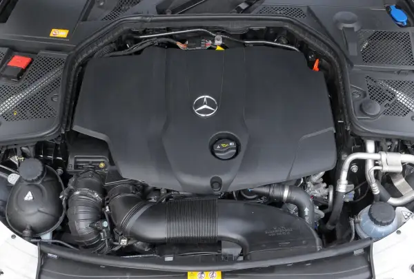 Silnik w Mercedesie C W205. Widoczna czarna osłona z logo producenta, przewody i elementy układu dolotowego.