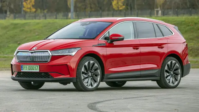 Czerwona Skoda Enyaq, elektryczny SUV, prezentuje się dynamicznie na tle zieleni.