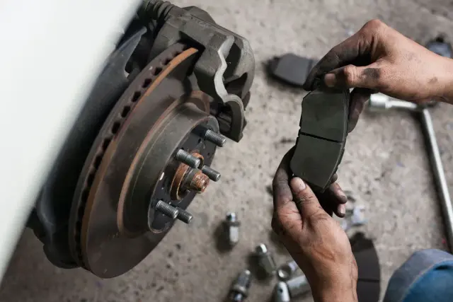 Mechanik pokazuje zużyte klocki hamulcowe przed wymianą. Widać tarczę hamulcową i zacisk.