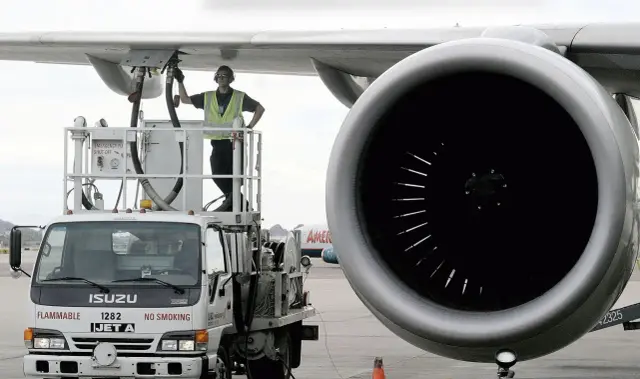 Pracownik na podnośniku tankuje samolot. Na ciężarówce napis "JET A", co może pomóc oszacować, ile kosztuje paliwo lotnicze.